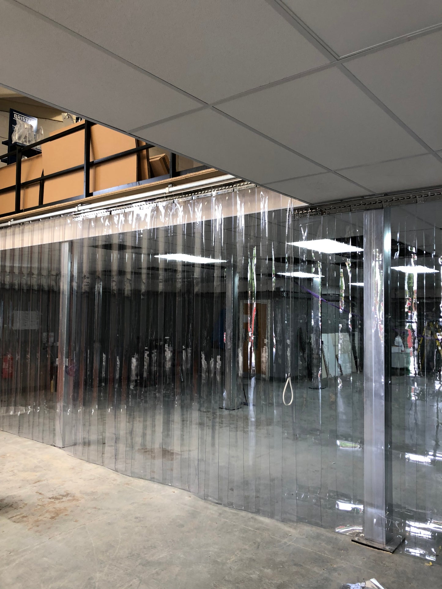 Clear PVC strip curtain door kit installed in a warehouse with overhead hook system
