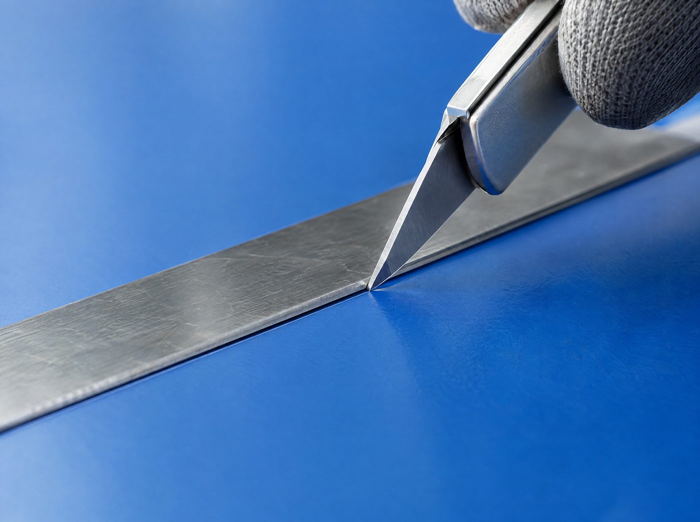 Safety knife making a shallow cut on a blue polyurethane mat along a steel straight edge
